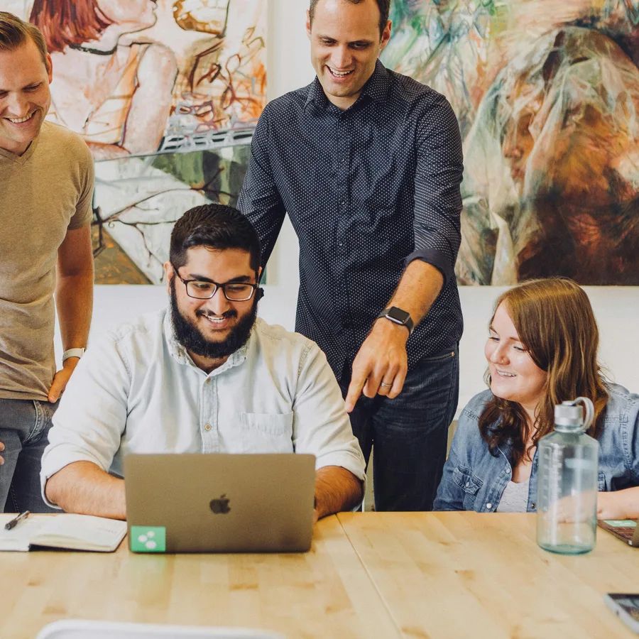 A diverse group of colleagues excitedly gathered around a laptop